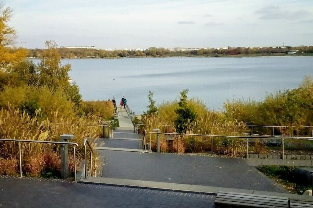 Ein Weg, der zu einem Gewässer führt und einen Blick auf entfernte Gebäude bietet.