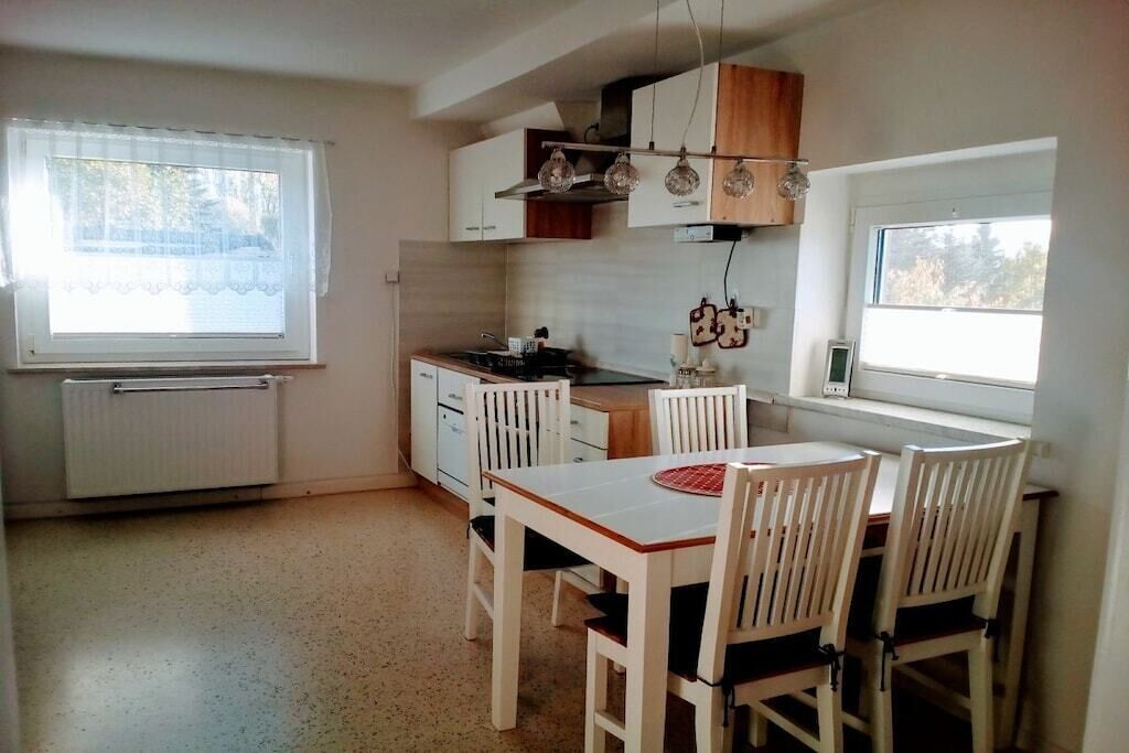 Cocina compacta con armarios blancos, una mesa de comedor con sillas y un ventanal que proporciona luz natural.