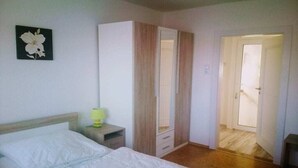 A bedroom with a bed, a wardrobe, a nightstand, and a door leading to another room.