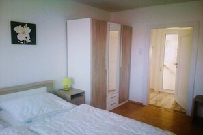 A bedroom with a bed, a wardrobe, a nightstand, and a door leading to another room.