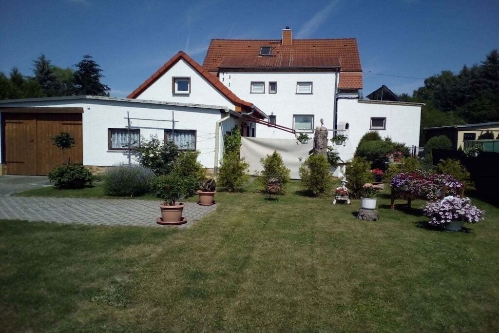 A two-story house with a red-tiled roof, a garage, and a well-maintained garden with various potted plants and flowers.