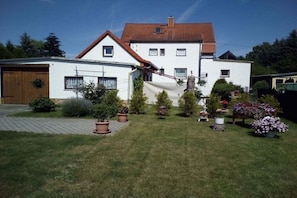 A two-story house with a red-tiled roof, a garage, and a well-maintained garden with various potted plants and flowers. - Holiday apartment with 2 bedrooms (Markranstädt)