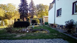 A residential backyard with a lawn, a small pond, a swing set, and a white building with windows.