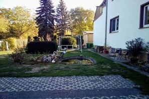 A residential backyard with a lawn, a small pond, a swing set, and a white building with windows.