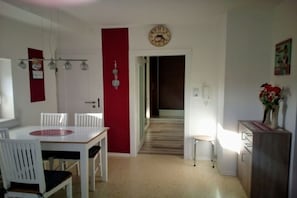 Ein Essbereich mit einem weißen Tisch und Stühlen, einer roten Akzentwand, einer Uhr und einem Flur, der in einen anderen Raum führt.