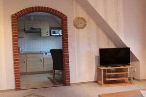 A compact living space with a kitchen area, a television on a stand, and a clock on the wall. - Holiday apartment with 1 bedroom (Norden-Norddeich)
