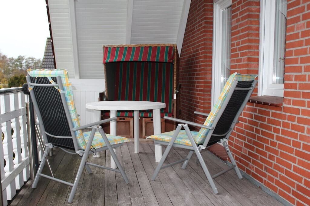 Un espacio de estar al aire libre techado con una mesa y dos sillas, una pared de ladrillo y una valla blanca.