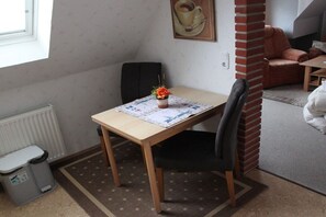 A small dining area with a table, chairs, a trash bin, and a radiator. - Holiday apartment with 1 bedroom (Norden-Norddeich)