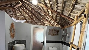 Ein Badezimmer mit Steinboden, einem weißen Waschbecken, einer Toilette und einer Bambusleiter.