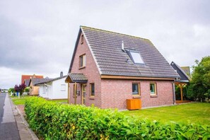 A single-story brick house with a sloped roof and a small attached garage. - Holiday home with 3 bedrooms (Wurster Nordseeküste)