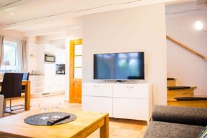 A modern living room with a flat-screen TV, a dining area with a table and chairs, and a staircase leading to an upper level. - Holiday home with 3 bedrooms (Wurster Nordseeküste)
