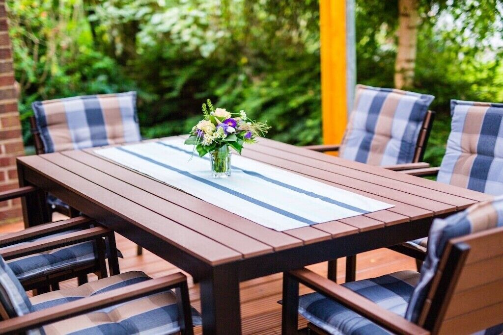 Une table en bois, recouverte d’un chemin de table blanc, entourée de chaises dotées de coussins à carreaux.