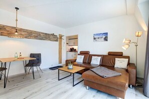 Ein modernes Wohnzimmer mit einem braunen Ledersofa, einem Holztisch, einem Esstisch mit Stühlen und einer Pendelleuchte.