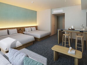 Habitación de hotel con dos camas, un escritorio con dos taburetes y una pequeña zona de estar.