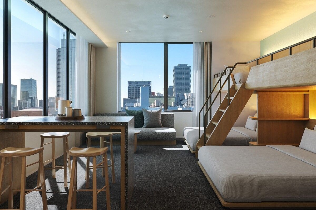 Una habitación de hotel moderna con vista a la ciudad, un escritorio con taburetes, un sofá y una cama litera.