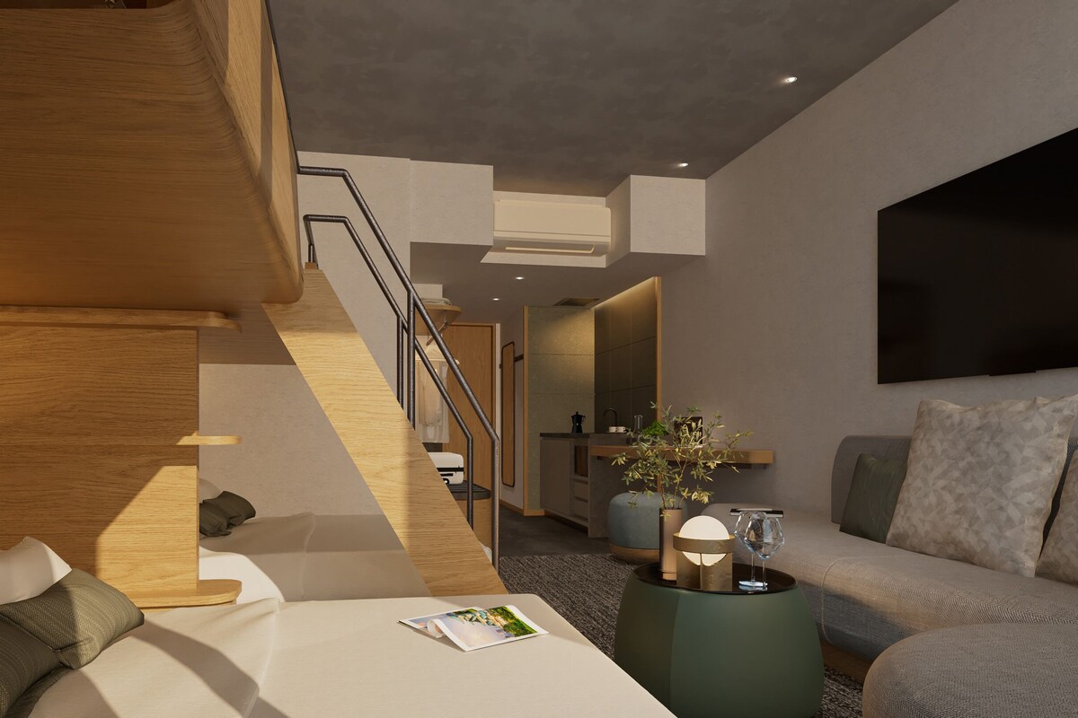 A modern hotel room with a wooden staircase, a sofa, a coffee table, and a flat-screen TV.