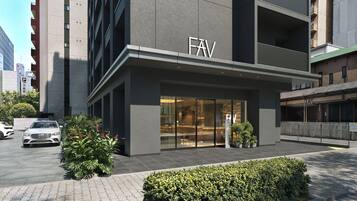 Un edificio moderno con un llamativo letrero 'FAV', entrada de vidrio y un área de estacionamiento con un coche blanco.