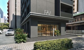 Un edificio moderno con un llamativo letrero 'FAV', entrada de vidrio y un área de estacionamiento con un coche blanco.