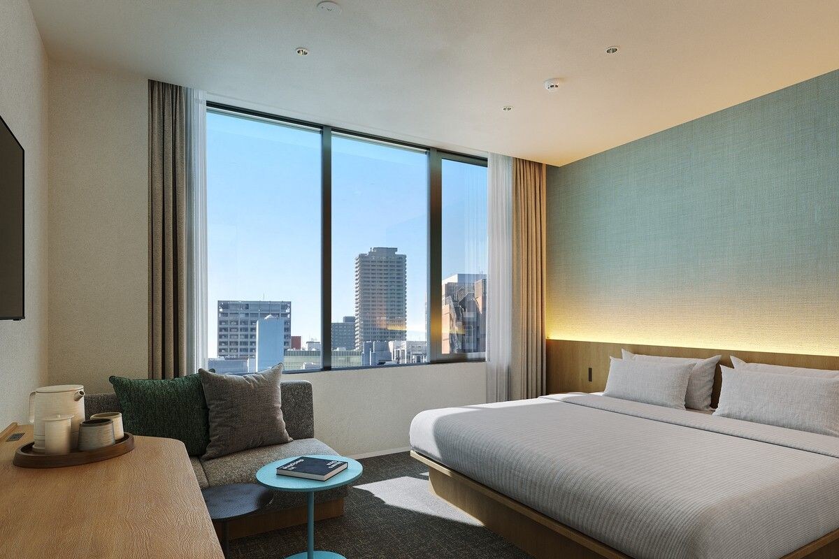 Una habitación de hotel con una cama grande, una zona de estar con una mesa y vistas a la ciudad a través de la ventana.