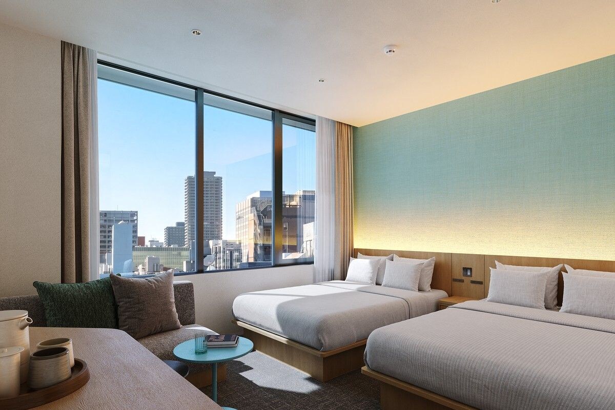 Habitación de hotel con dos camas, un sofá, una mesita y vistas a la ciudad.