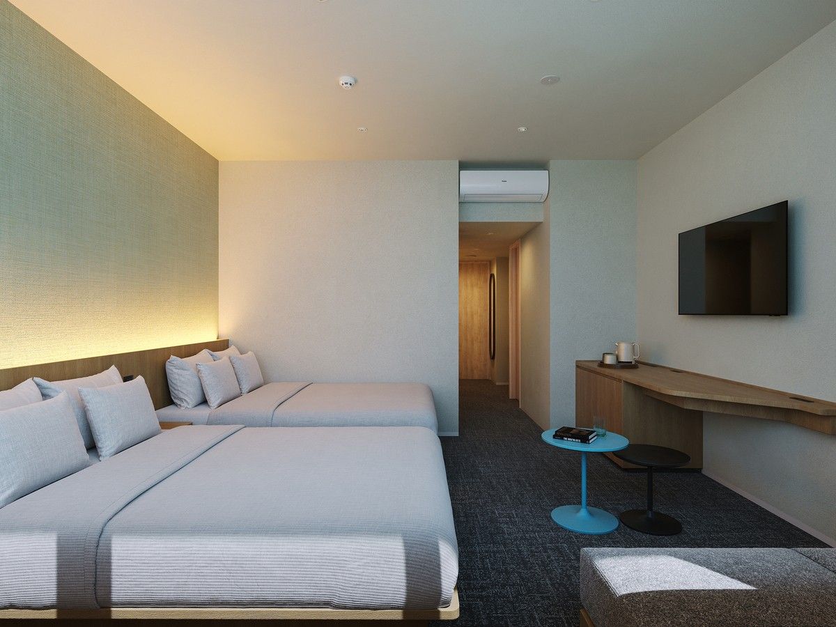 A hotel room with two beds, a TV mounted on the wall, a small table with a cup, and a desk with a chair.
