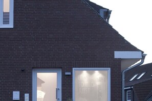 A brick building with a large glass door and a sign that reads 'UTS TO HIS JUST'. - "Sandplaat" in Uns to Hus (Juist)