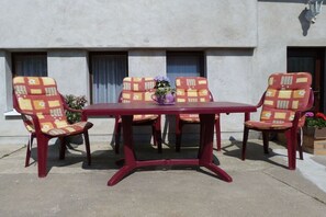 A table with four chairs, each with a patterned cushion, in front of a building with windows and a door. - Holiday apartment with 2 bedrooms (Stubbenfelde)