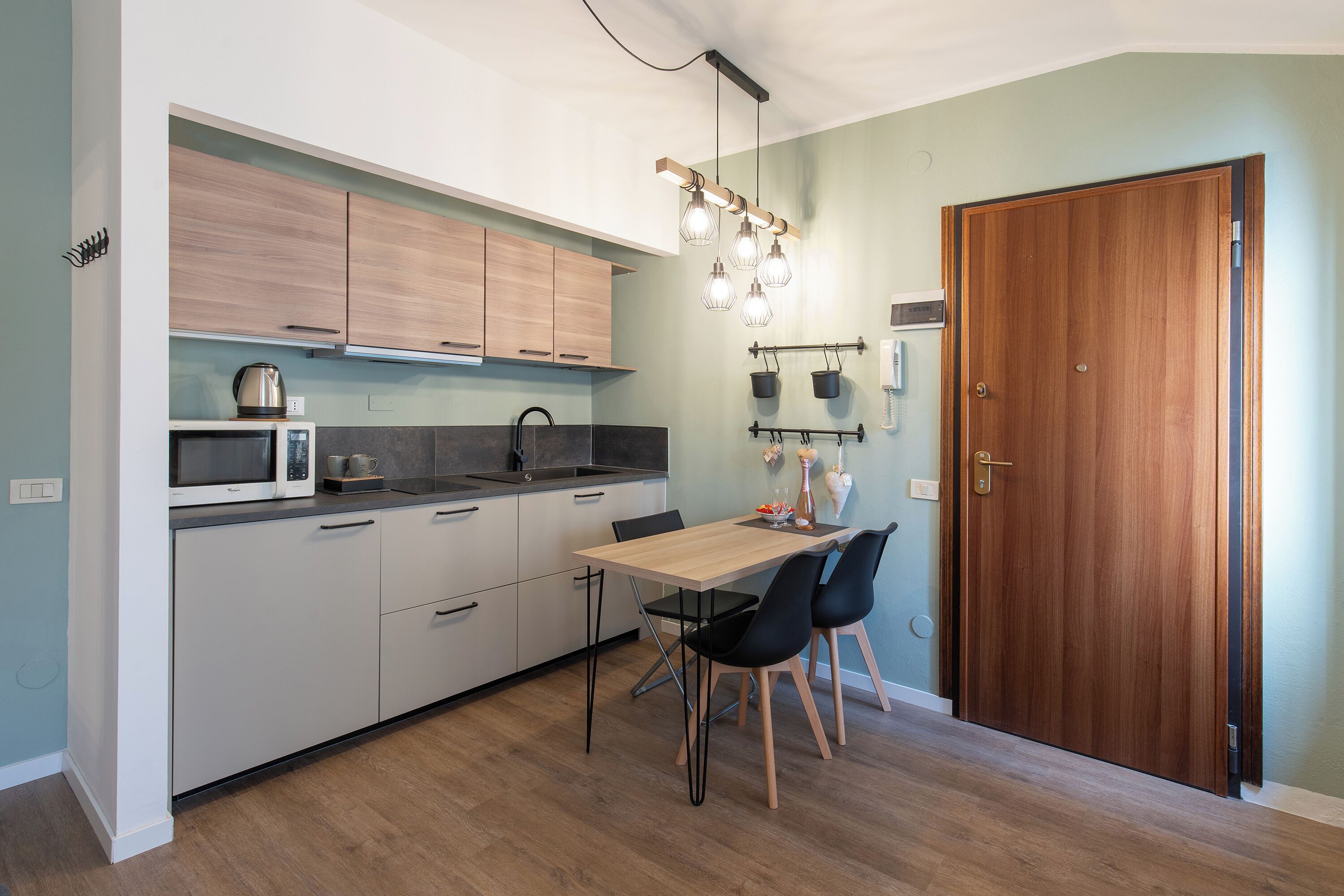 A compact kitchen with a dining area, wooden cabinets, a microwave, and a hanging light fixture.