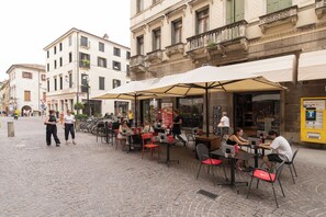 An outdoor café with tables and chairs, a menu board, and a building with a balcony in the background. - EnJoy Home - Two-room apartment in a prime location on Via Roma (Padova)