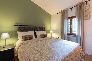 A bedroom with a bed, two bedside tables, a nightstand, a window with curtains, and a wall-mounted radiator. - EnJoy Home - Two-room apartment in a prime location on Via Roma (Padova)