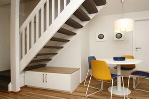 A staircase with white railings and wooden steps, a white dining table with yellow chairs, and a wall-mounted lamp. - "Füürtoorn" at Uns to Hus (Juist)