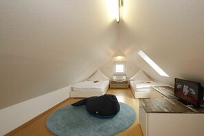A small, triangular attic bedroom with two beds, a television, and a window. - "Füürtoorn" at Uns to Hus (Juist)