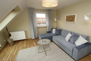 A modern living room with a grey sofa, a small round table, and a window with curtains. - "Füürtoorn" at Uns to Hus (Juist)