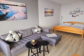 Ein modernes Schlafzimmer mit einem grauen Sofa, einem hölzernen Bett und einem kleinen runden Tisch mit einer Obstschale.