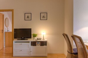 A room with a television on a white cabinet, a lamp, two framed pictures on the wall, and a chair. - at the Fock fruit farm - Hofblick (Mittelnkirchen)