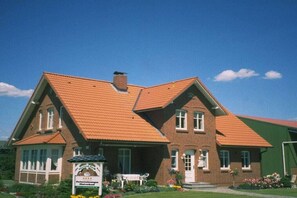 A two-story brick building with a red-tiled roof, a signboard, and a bench in front. - at the Fock fruit farm - Hofblick (Mittelnkirchen)