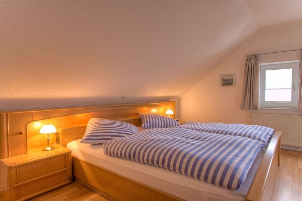 A bedroom with a single bed, wooden headboard, bedside lamps, and a window with curtains.