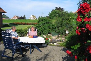 Two people seated at an outdoor table with a white tablecloth, surrounded by greenery and a garden. - at the Fock fruit farm - Hofblick (Mittelnkirchen)