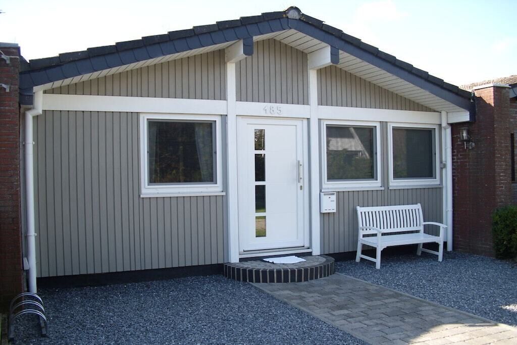 Een gebouw met een grijze gevel, een witte deur met het nummer 185, en een bankje ervoor.