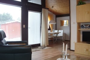 A living room with a sofa, a dining area with a table and chairs, and a television on a wooden cabinet. - Holiday home with 2 bedrooms (Butjadingen)