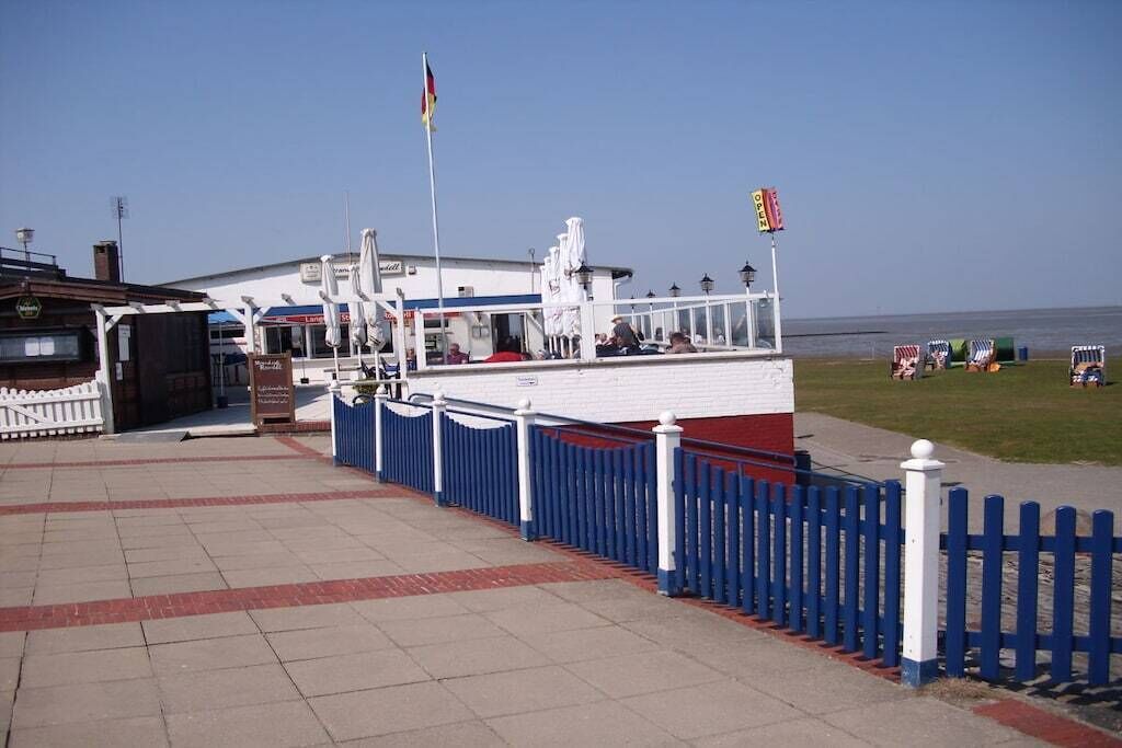 A waterfront building with a white facade, a blue and white fence, and a flagpole.
