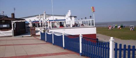 A waterfront building with a white facade, a blue and white fence, and a flagpole.
