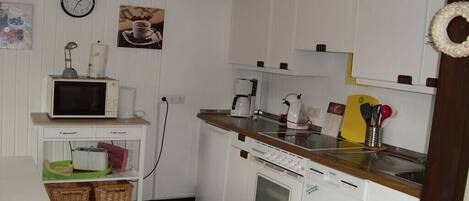 A compact kitchen with a microwave, stove, and coffee maker. There are baskets on a shelf and a clock on the wall.