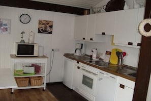 A compact kitchen with a microwave, stove, and coffee maker. There are baskets on a shelf and a clock on the wall. - Holiday home with 2 bedrooms (Butjadingen)