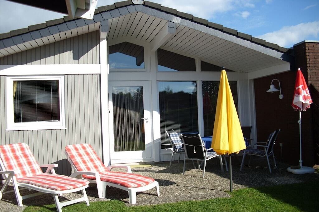 Een overdekt terras met twee loungestoelen, een gele parasol en een tafel met stoelen.