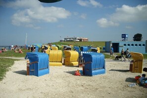 A beach with beach chairs and umbrellas, a building in the background, and a clear sky. - Holiday home with 2 bedrooms (Butjadingen)