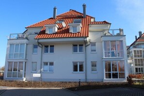 Ein mehrstöckiges Wohngebäude mit rotem Ziegeldach, zahlreichen Fenstern und Balkonen.