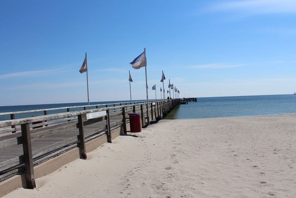 Eine Holzstege, der sich in einen sandigen Strand erstreckt, mit Flaggenabständen.