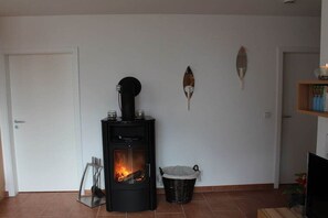 Een kamer met een houtkachel, een deur, een decoratief object aan de muur en een mand.