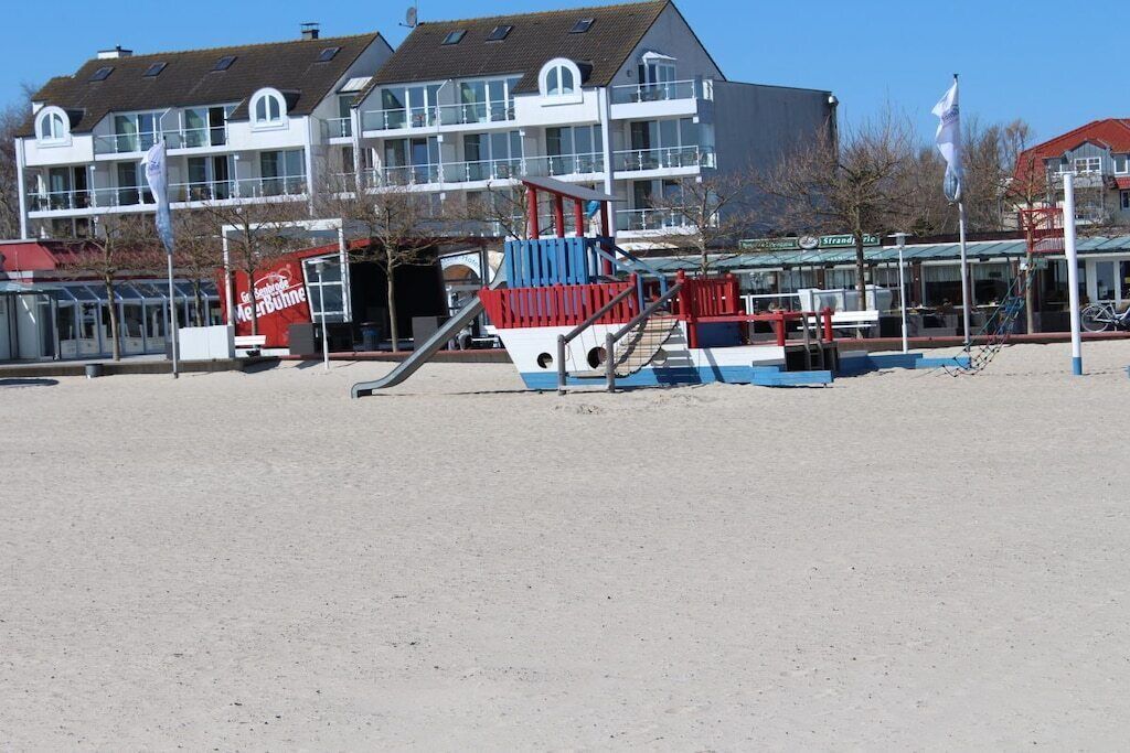 A beachside playground with a slide and climbing structures, a building with multiple windows, and a flagpole.